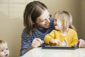 Father (30s) playing with daughter (2 years) who has down syndrome. Using digital tablet.